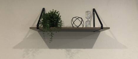 Een houten plank met een potplant, twee zandlopers en een opgerolde draadsculptuur, geplaatst tegen een effen muur.