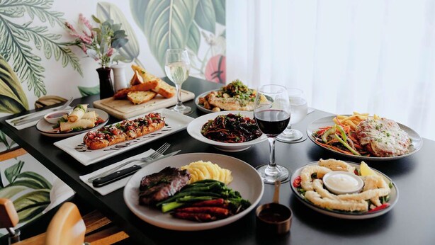 Una mesa de comedor con diversos platos y bebidas, con un gran estampado botánico de fondo.
