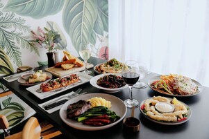 Una mesa de comedor con diversos platos y bebidas, con un gran estampado botánico de fondo.