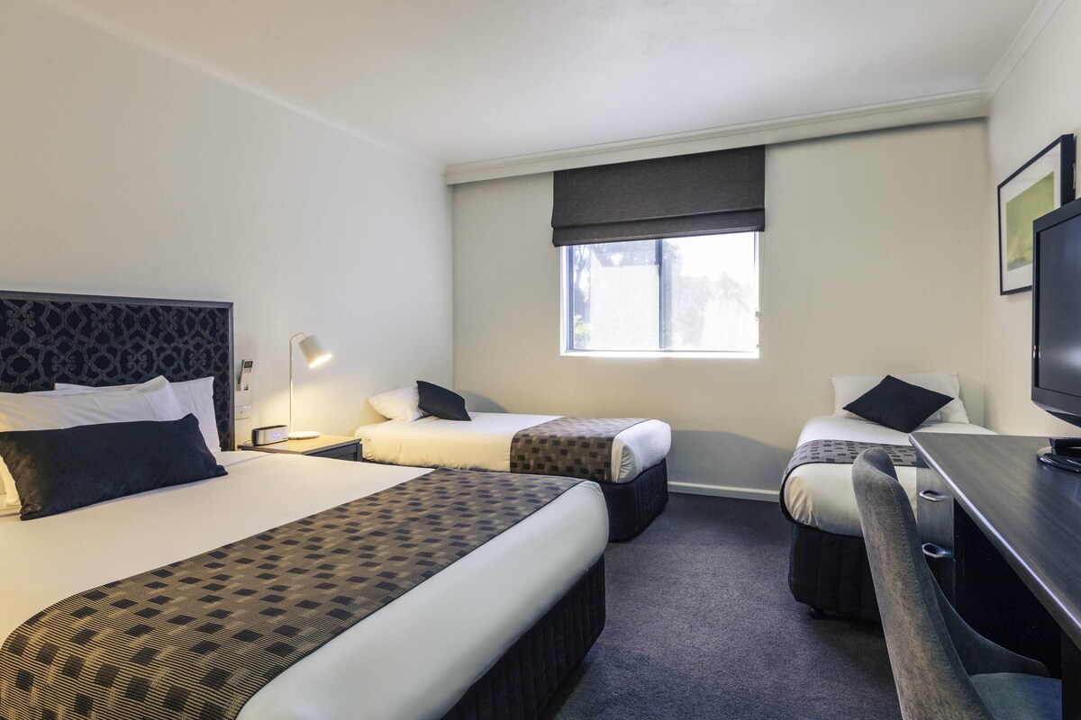 Habitación de hotel con dos camas, un escritorio, una silla, un televisor y una ventana.