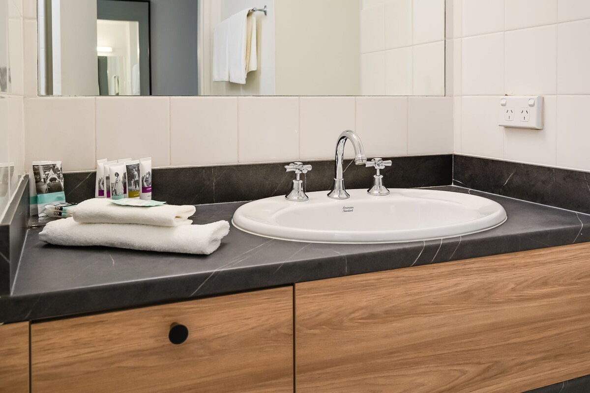 A modern bathroom with a large mirror, white sink, and wooden vanity.