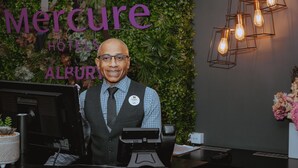 Un comptoir d’accueil d’hôtel avec une plaque nominative, un ordinateur et une plante.