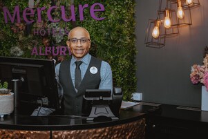 Mostrador de recepción de hotel con una placa, una computadora y una planta.