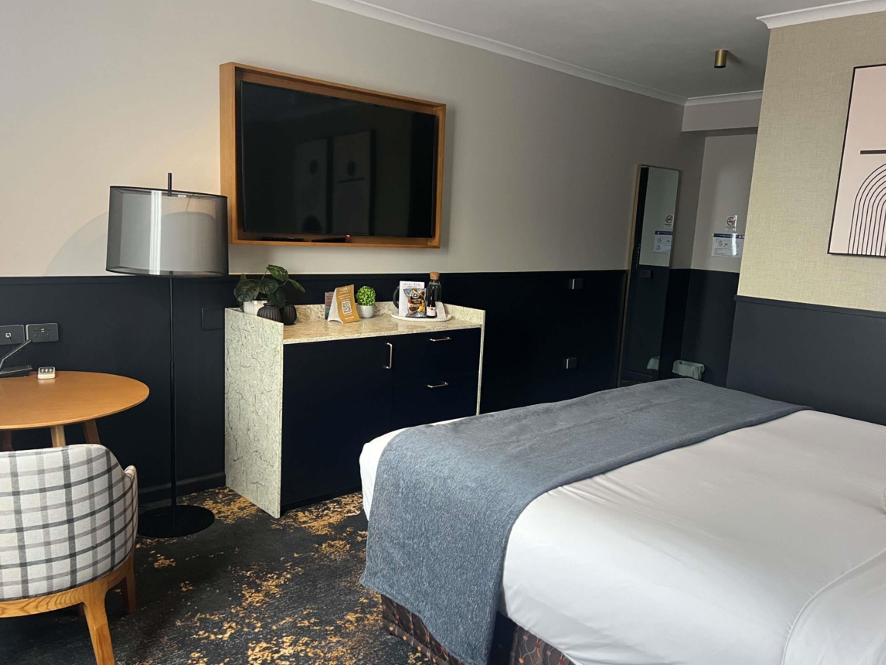 Une chambre d’hôtel avec un lit, un bureau, une chaise, un miroir et une petite table.