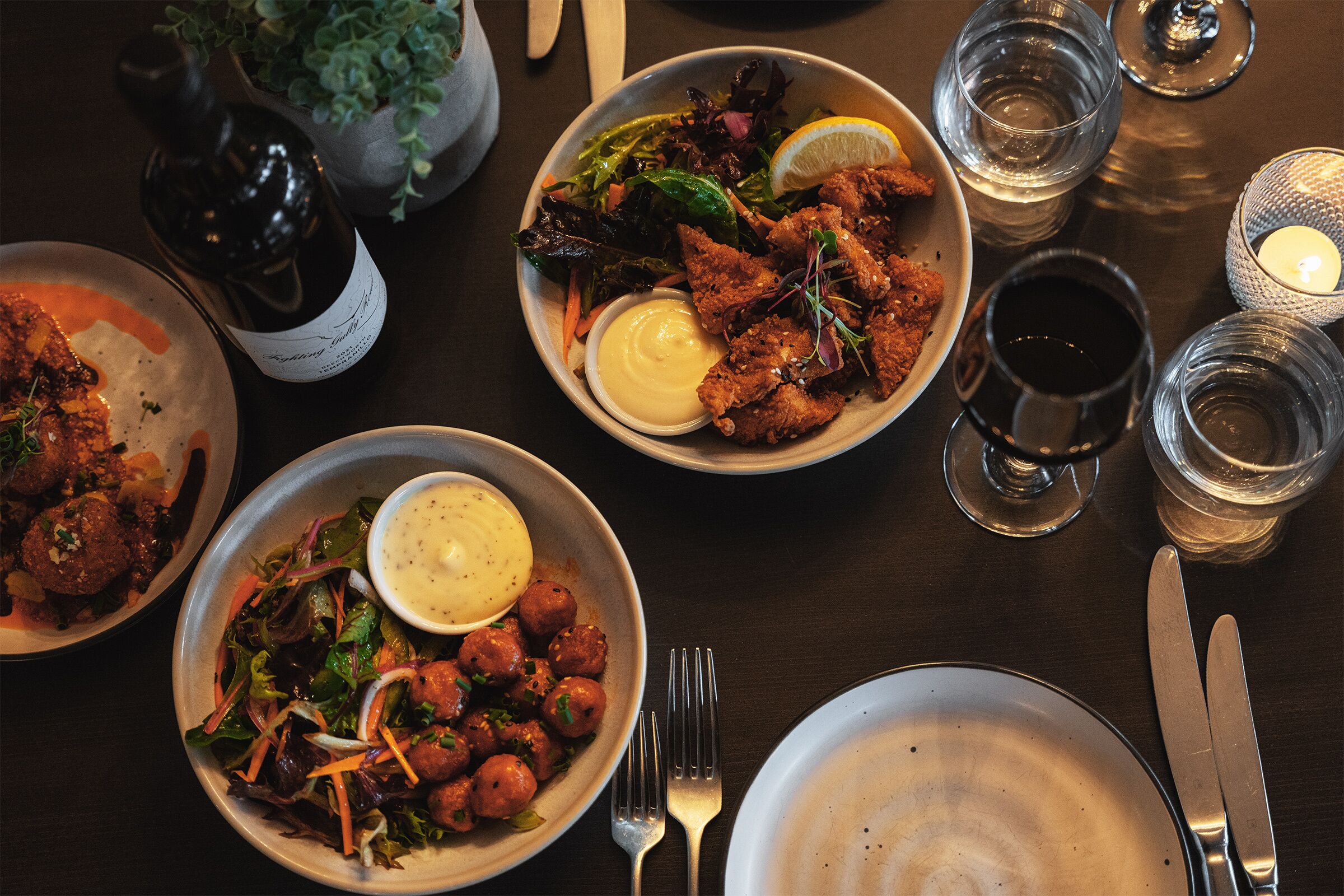 Una mesa de comedor con varios platos, incluyendo albóndigas, ensaladas y una botella de vino.