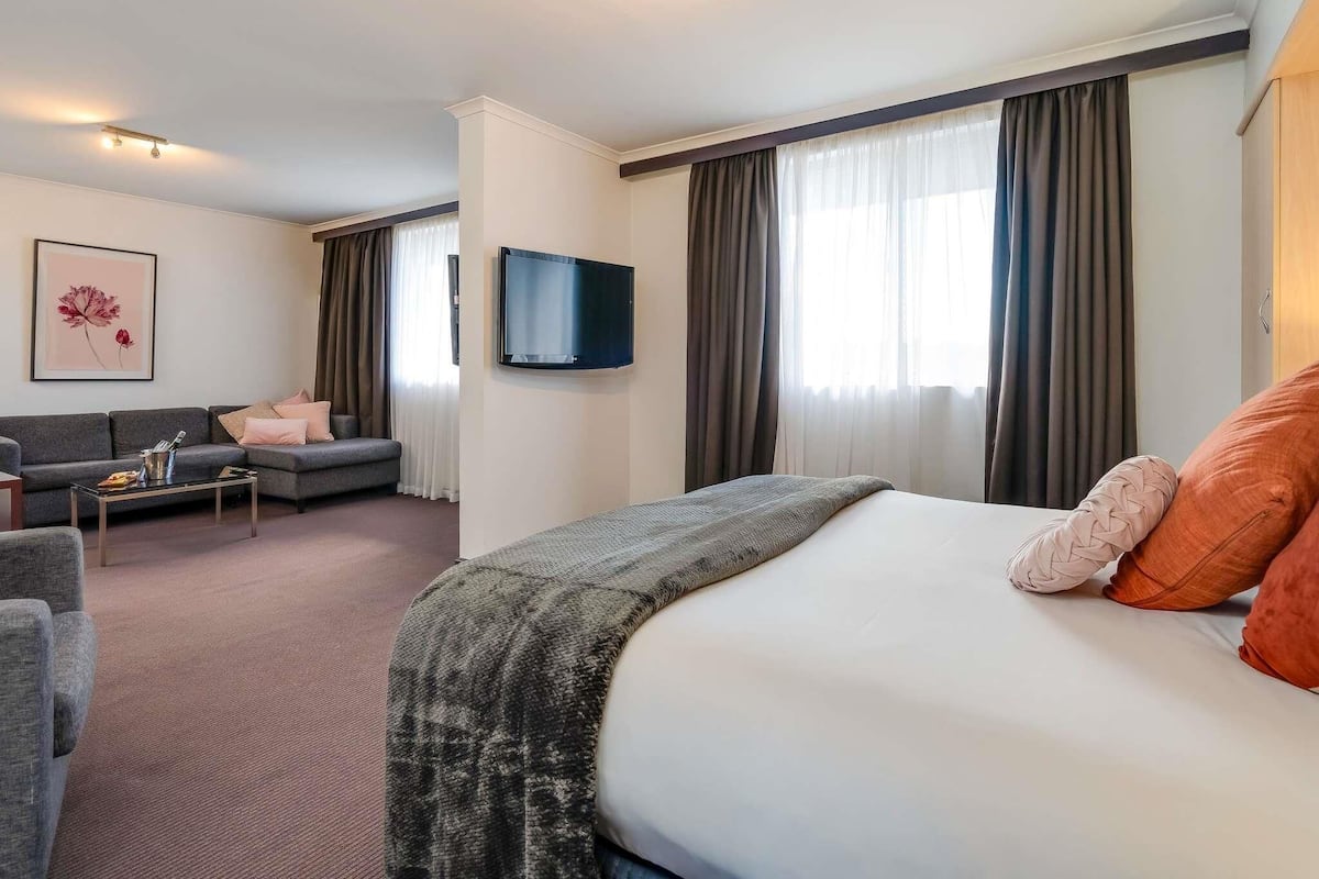 Una habitación de hotel con una cama, un sofá, un televisor y un cuadro en la pared.