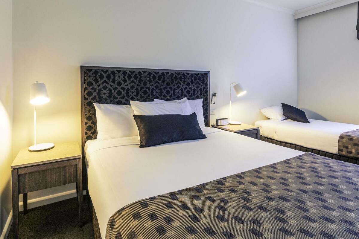 Habitación de hotel con una cama grande, dos mesitas de noche, un cabecero con diseño geométrico y un edredón estampado.