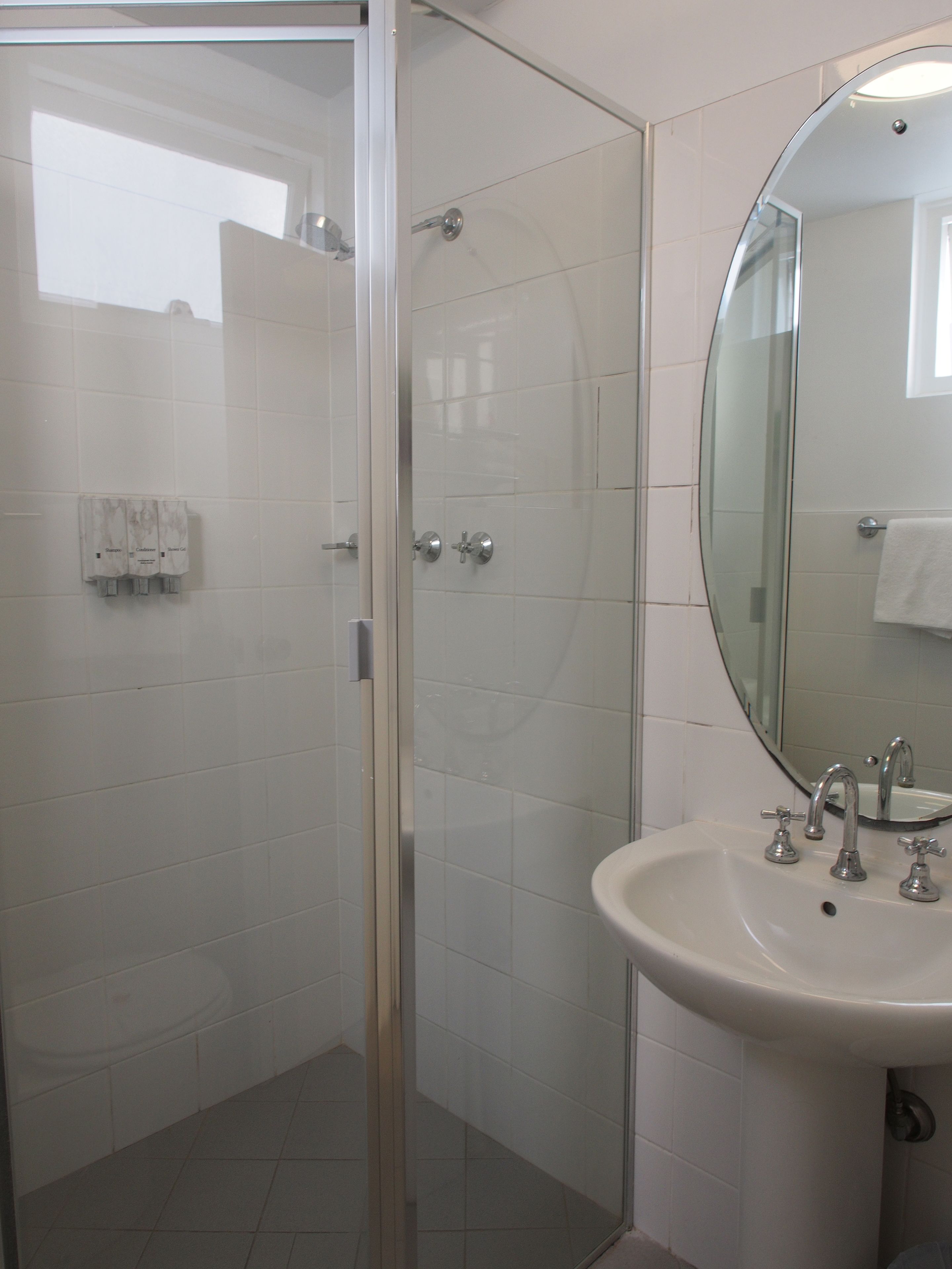 Un baño con cabina de ducha de vidrio, un lavabo con dos grifos y un espejo sobre el lavabo.