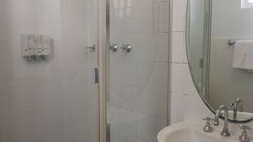 Un baño con cabina de ducha de vidrio, un lavabo con dos grifos y un espejo sobre el lavabo.