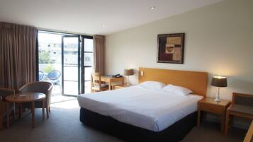 A hotel room with a large bed, a desk, a chair, and a view of the outside.