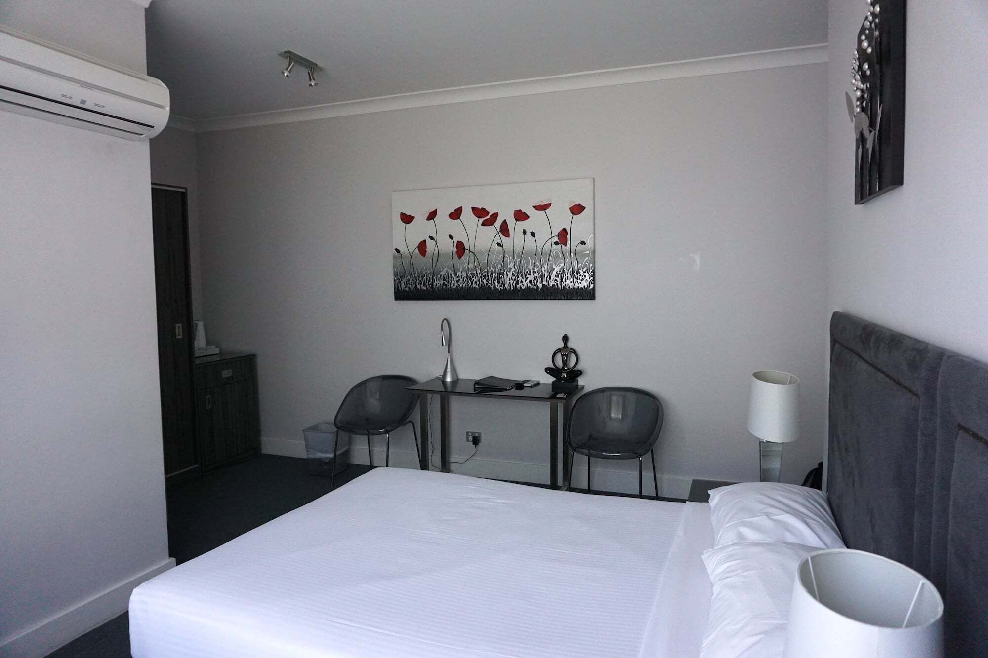 Una habitación de hotel con una cama, dos sillas, un escritorio, una lámpara y un cuadro en la pared.
