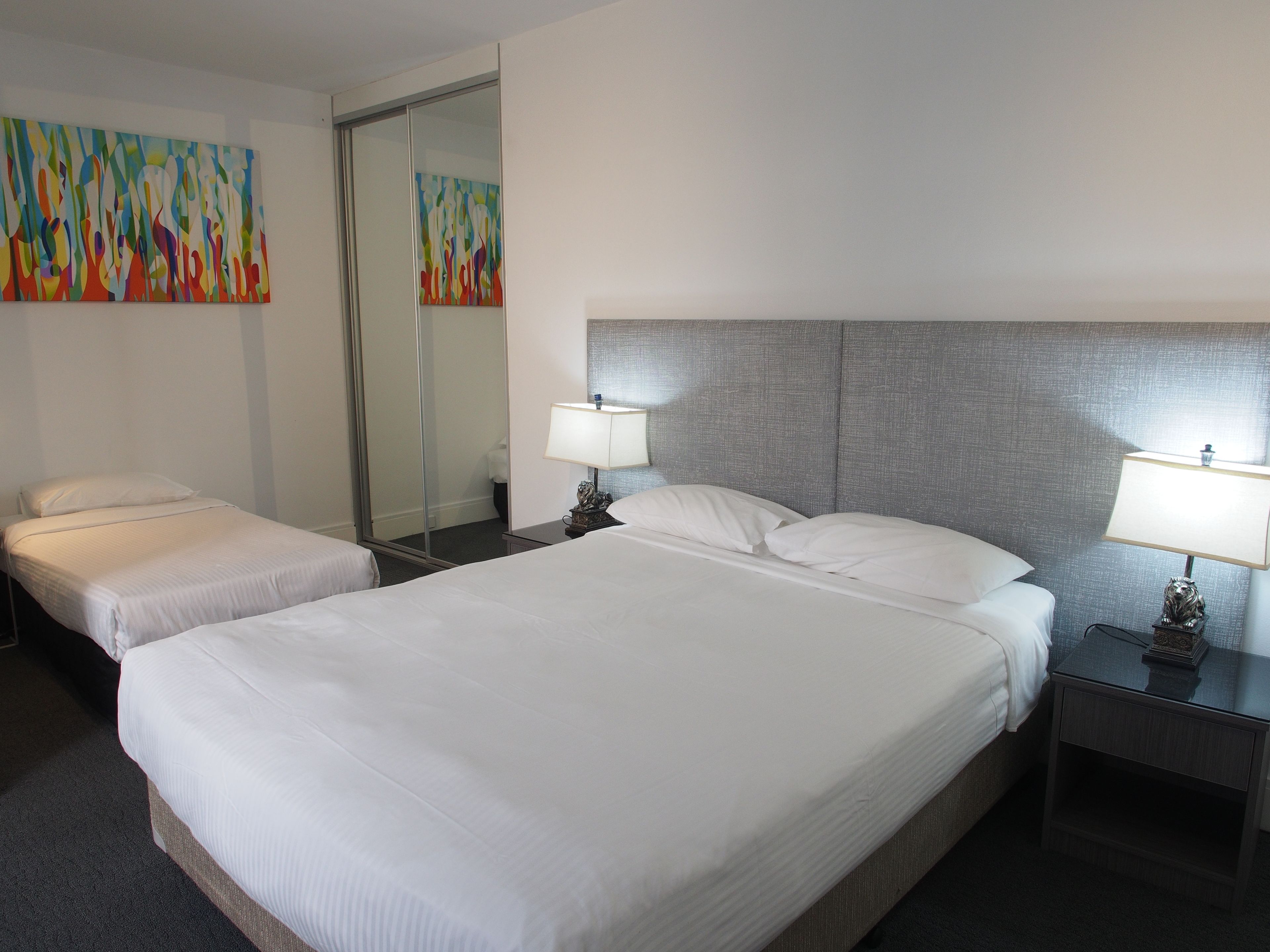 A hotel room with two beds, a large mirror, and a colorful abstract painting on the wall.