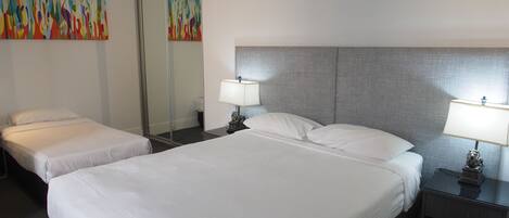 A hotel room with two beds, a large mirror, and a colorful abstract painting on the wall.