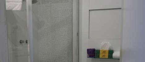 Un baño con ducha acristalada, inodoro blanco y estante con artículos de aseo.