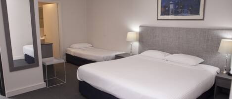 Habitación de hotel con dos camas, un espejo, un cuadro enmarcado en la pared y una mesita de noche con una lámpara.