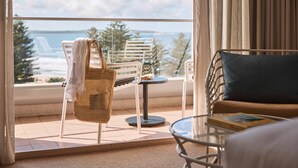 Ein Balkon mit Meerblick, ein Korbstuhl, ein kleiner runder Tisch und eine Couch mit Kissen.
