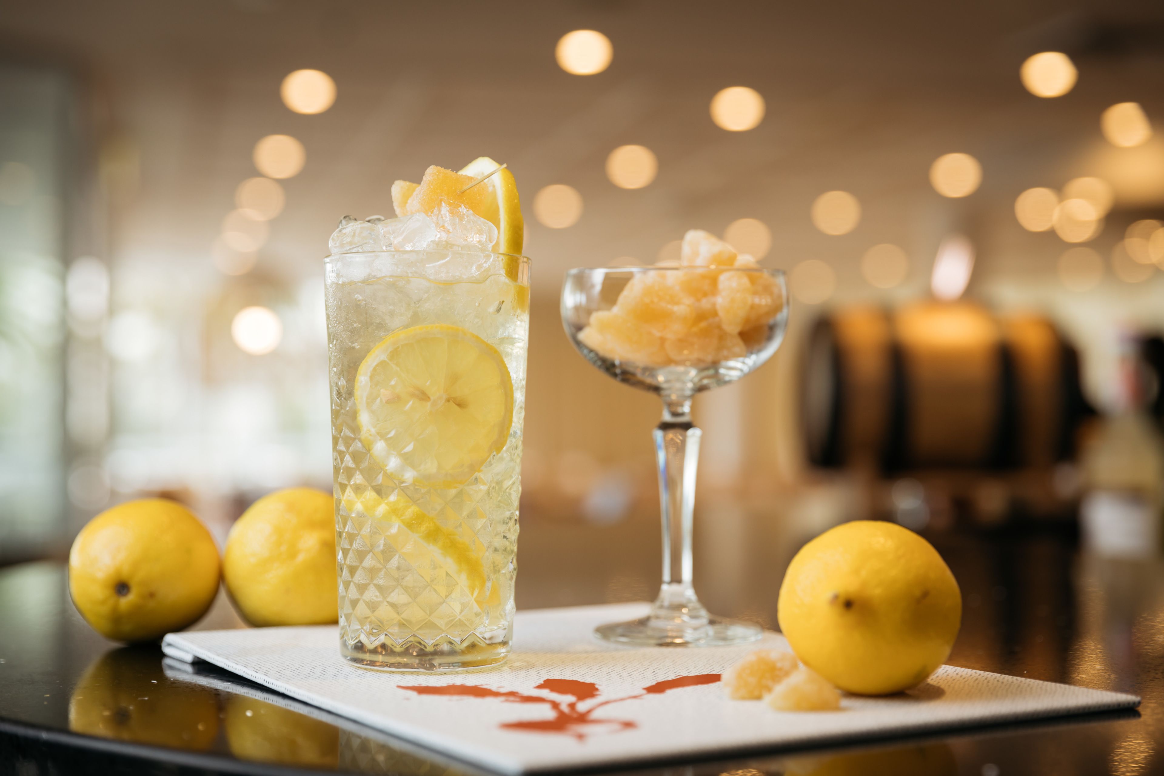 A glass of iced beverage with lemon slices, a small bowl of sugar, and lemons on a table.