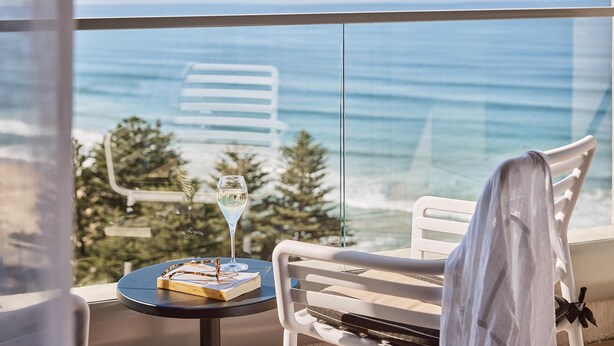 Ein Balkon mit Blick auf das Meer, ein Tisch mit Buch und Glas sowie ein weißer Stuhl.