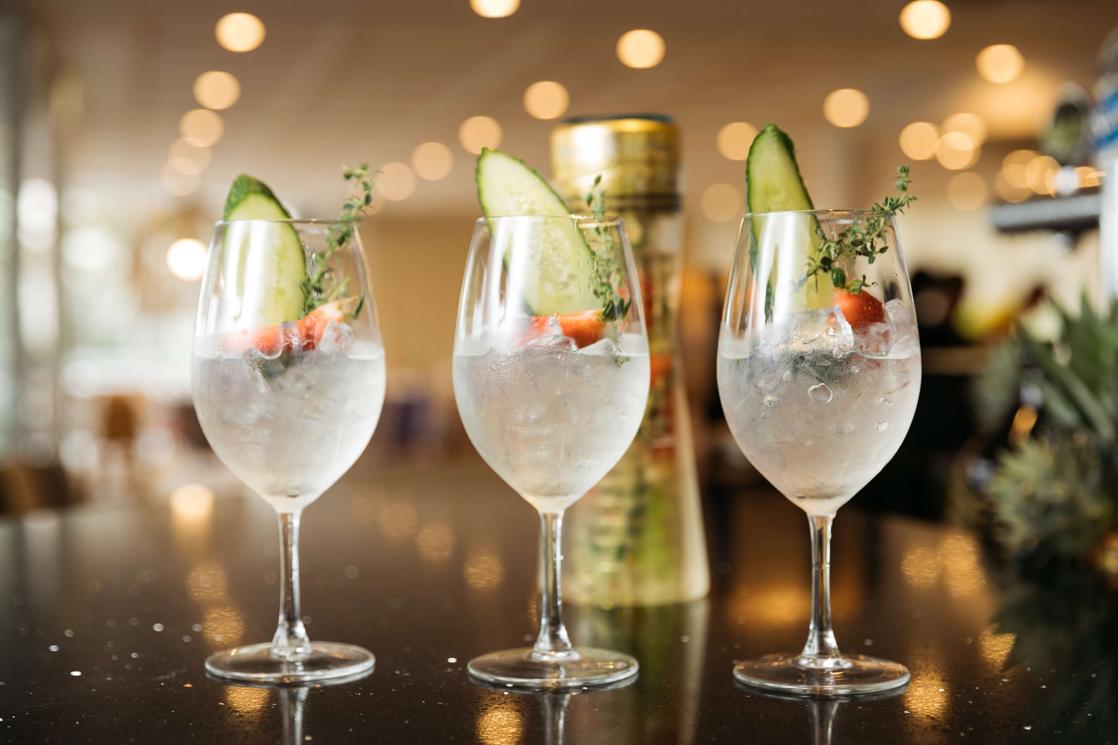 Three glasses of a cocktail with ice and garnishes on a bar counter.