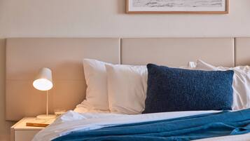 A neatly made bed with white and blue pillows, a blue blanket, and a bedside lamp on a nightstand with a book and glass.