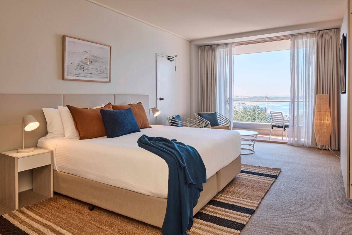 Een hotelkamer met een groot bed, een nachtkastje, een bureau, een stoel, een balkon met uitzicht en een lamp.
