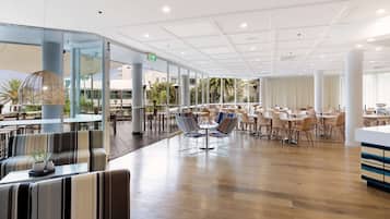 A spacious indoor dining area with multiple tables and chairs, large windows, and a modern ceiling design.