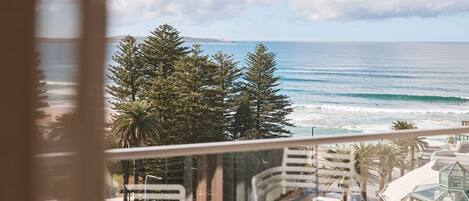 A view of the ocean with waves, a clear sky, and a street with trees and buildings.