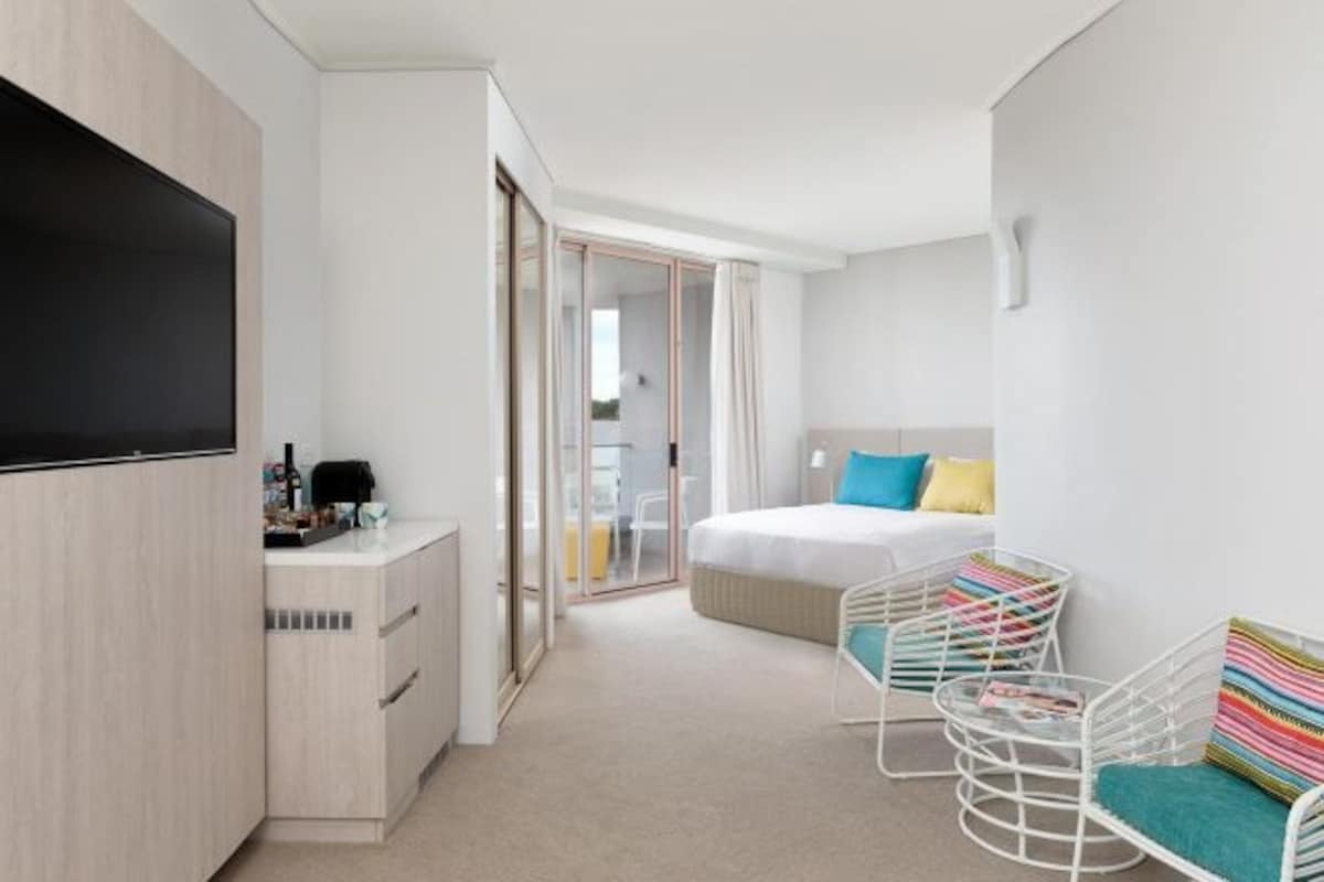 Una habitación de hotel moderna con una cama, un escritorio, un televisor y una zona de estar con sillas.