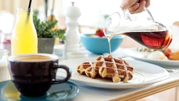 Ein Frühstücksbuffet mit Waffeln, Sirup, Kaffee und Fruchtsaft.