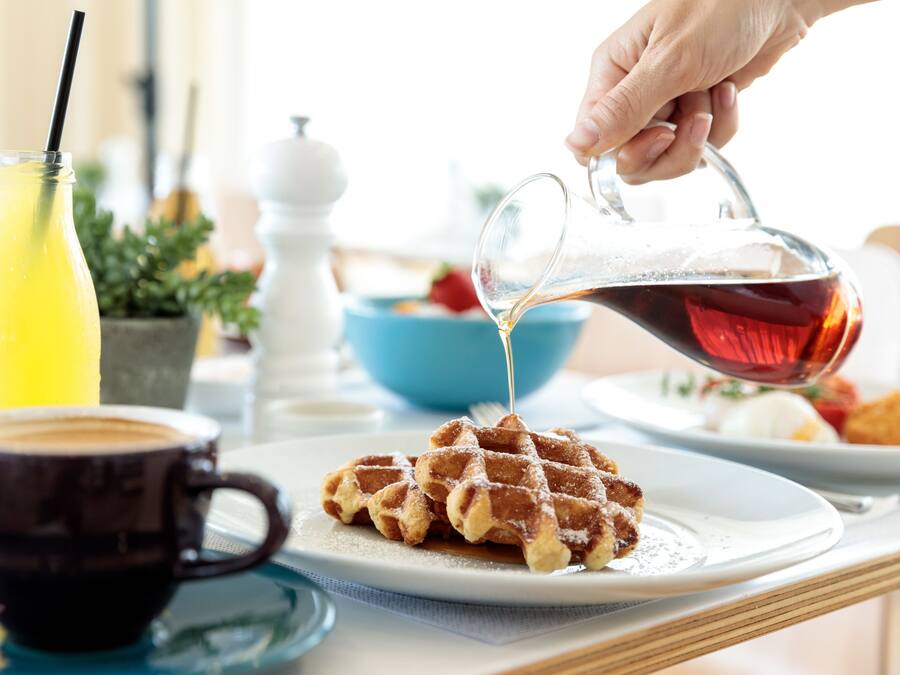 Ein Frühstücksbuffet mit Waffeln, Sirup, Kaffee und Fruchtsaft.