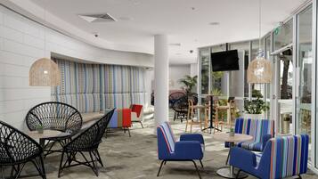 Uma área de lounge moderna com diversos assentos, incluindo cadeiras e sofás, uma mesa redonda e uma grande janela com vista para o exterior.