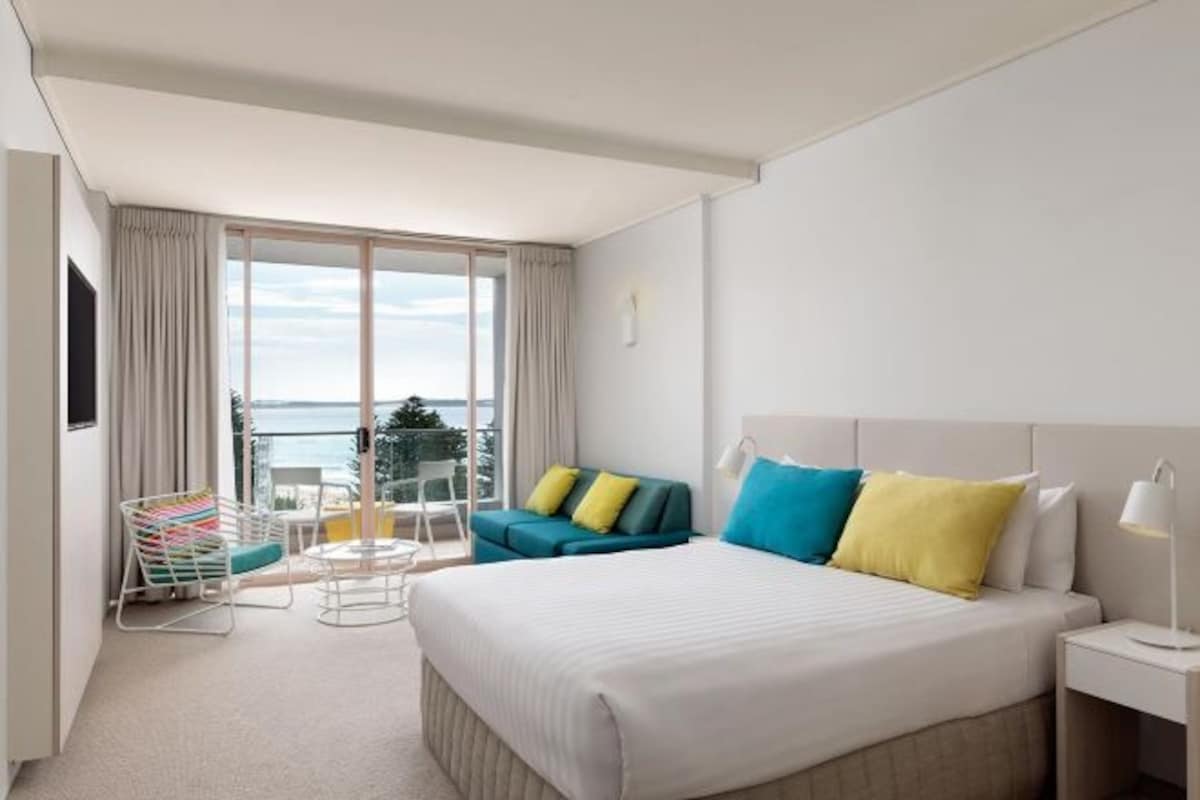 Habitación de hotel con una cama grande, un sofá, una silla y un balcón con vistas.