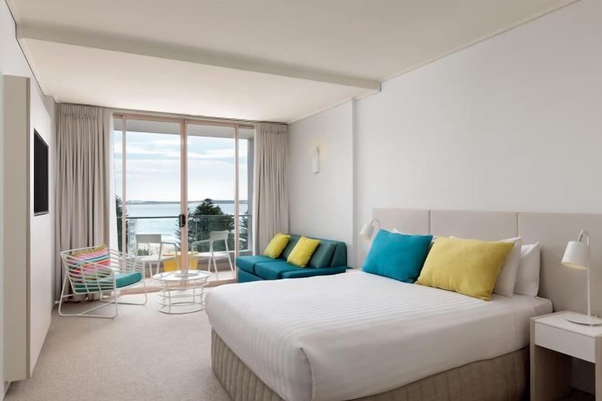 Habitación de hotel con una cama grande, un sofá, una silla y un balcón con vistas.