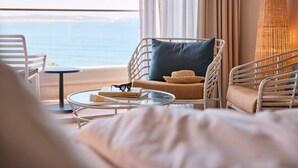 Ein modernes Hotelzimmer mit Meerblick, ausgestattet mit Korbmöbeln, einem Glastisch und einer gemütlichen Sitzecke.