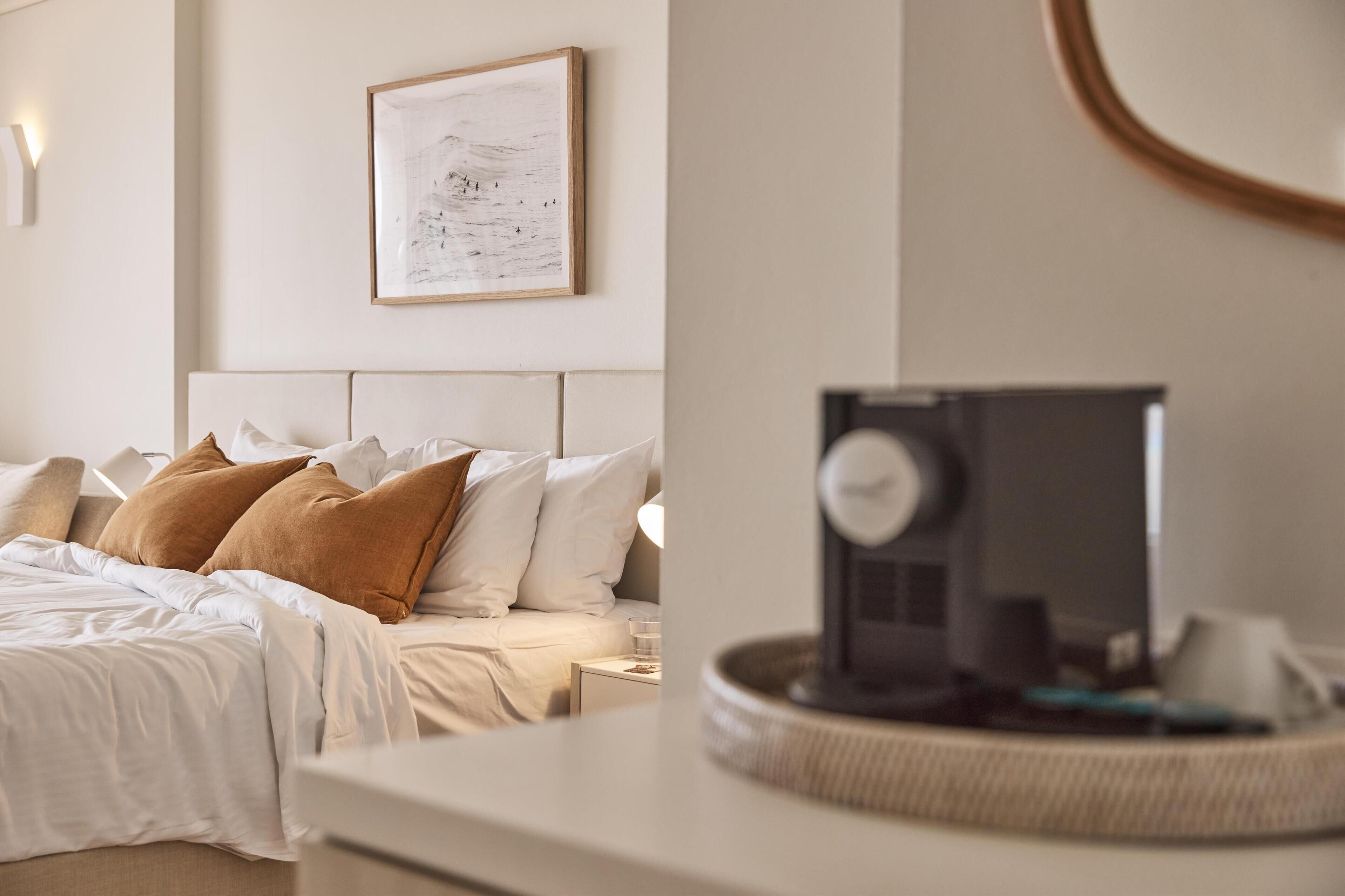 A neatly made bed with white and brown pillows, a framed artwork on the wall, and a bedside table with a lamp.