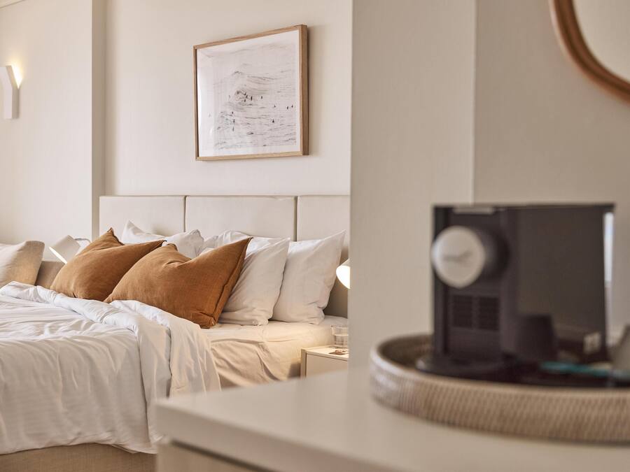 A neatly made bed with white and brown pillows, a framed artwork on the wall, and a bedside table with a lamp.
