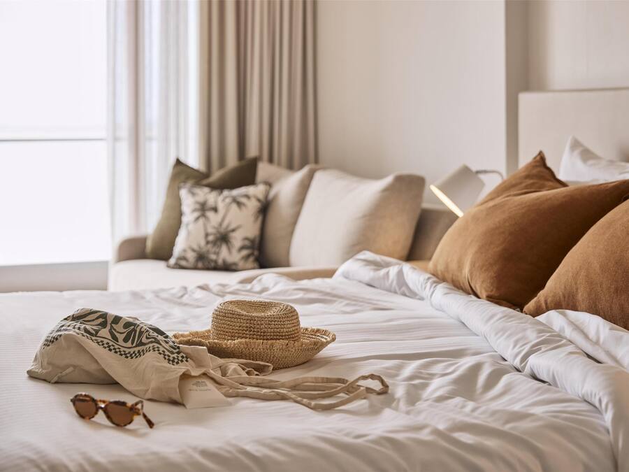 Una cama bien tendida con un sombrero de paja, gafas de sol y un tejido estampado.
