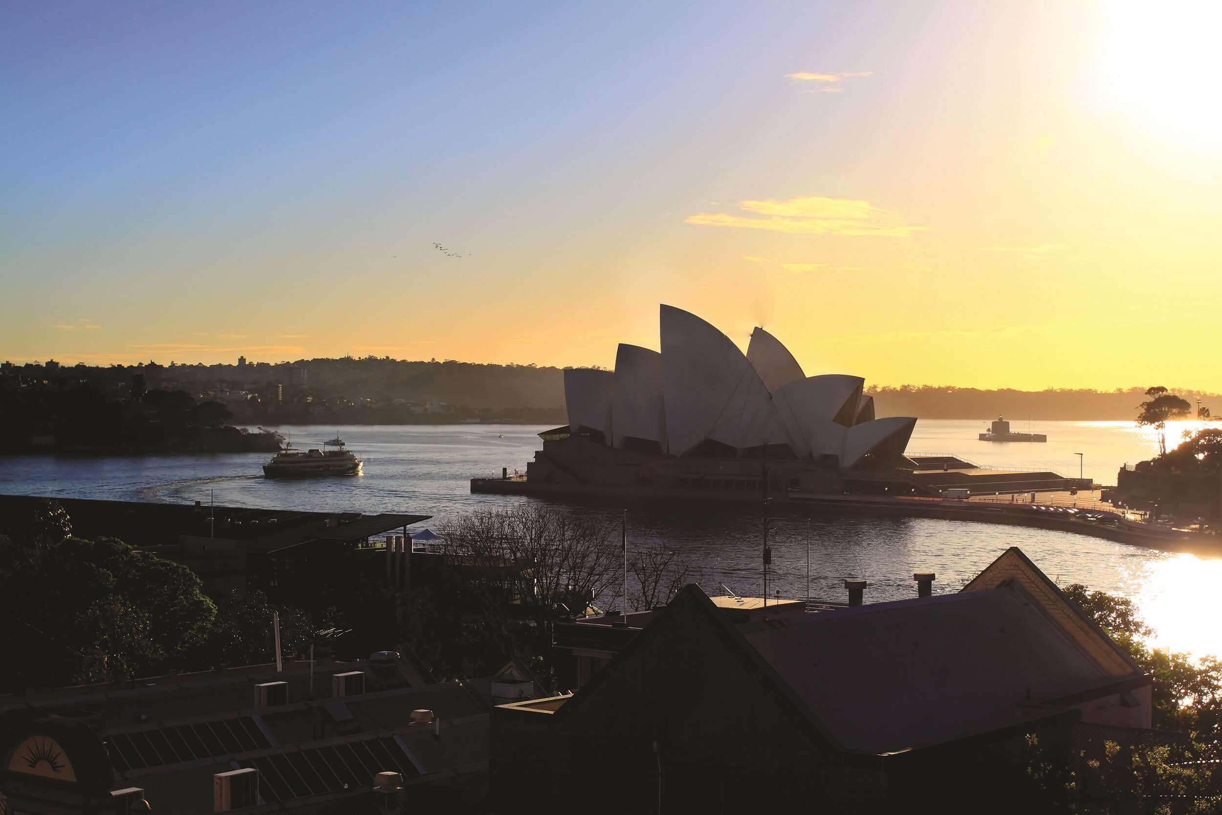 Ein Blick auf das Sydney Opera House bei Sonnenuntergang, im Hintergrund die Sydney Harbour Bridge.