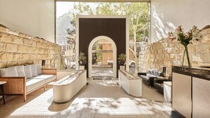 A modern lobby with a stone wall, a reception desk, seating areas, and a view through an archway. - Rendezvous Hotel Sydney The Rocks (The Rocks)
