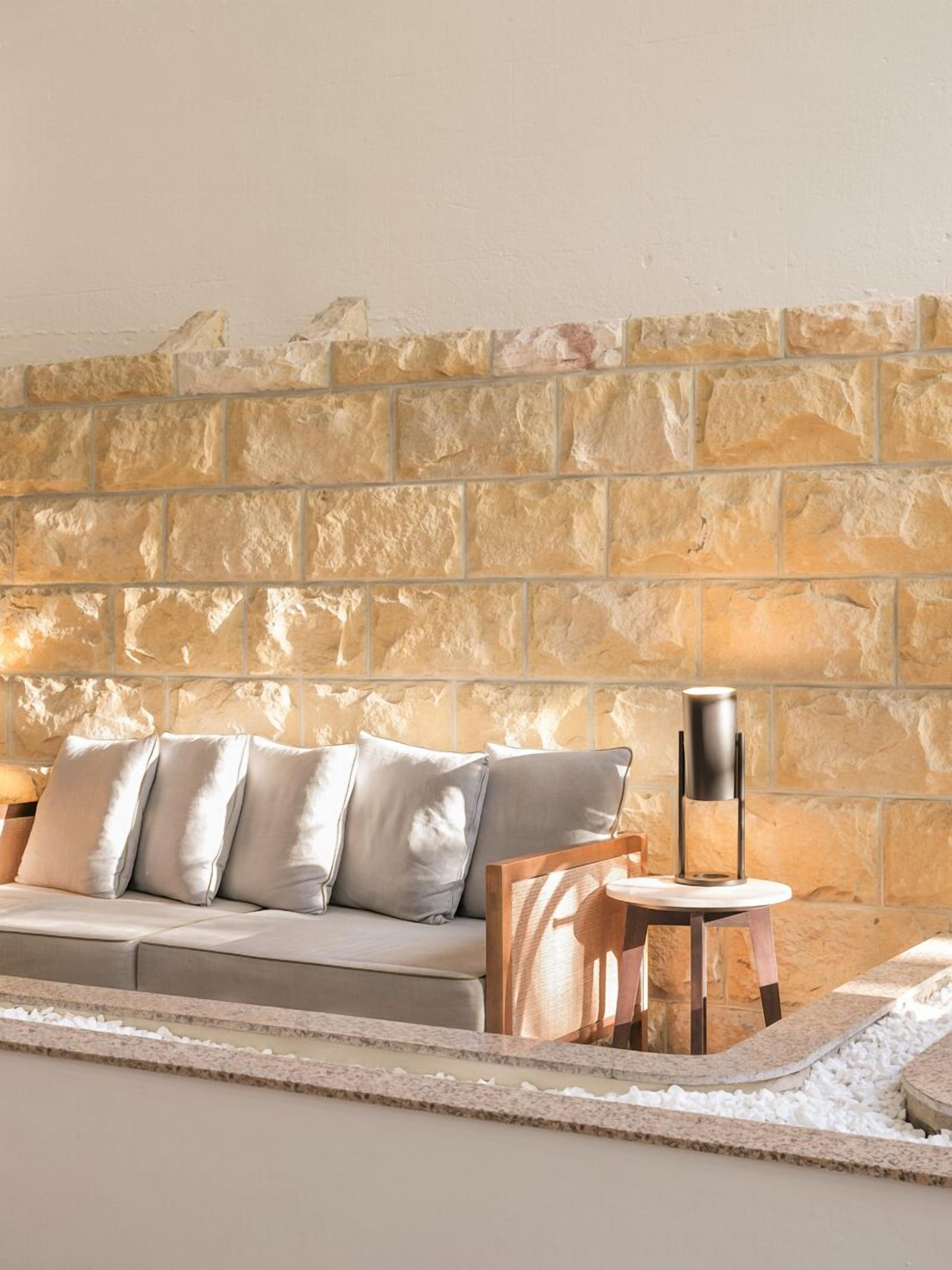 A modern living room with a stone wall, a sofa with cushions, a small wooden table, and a floor lamp.