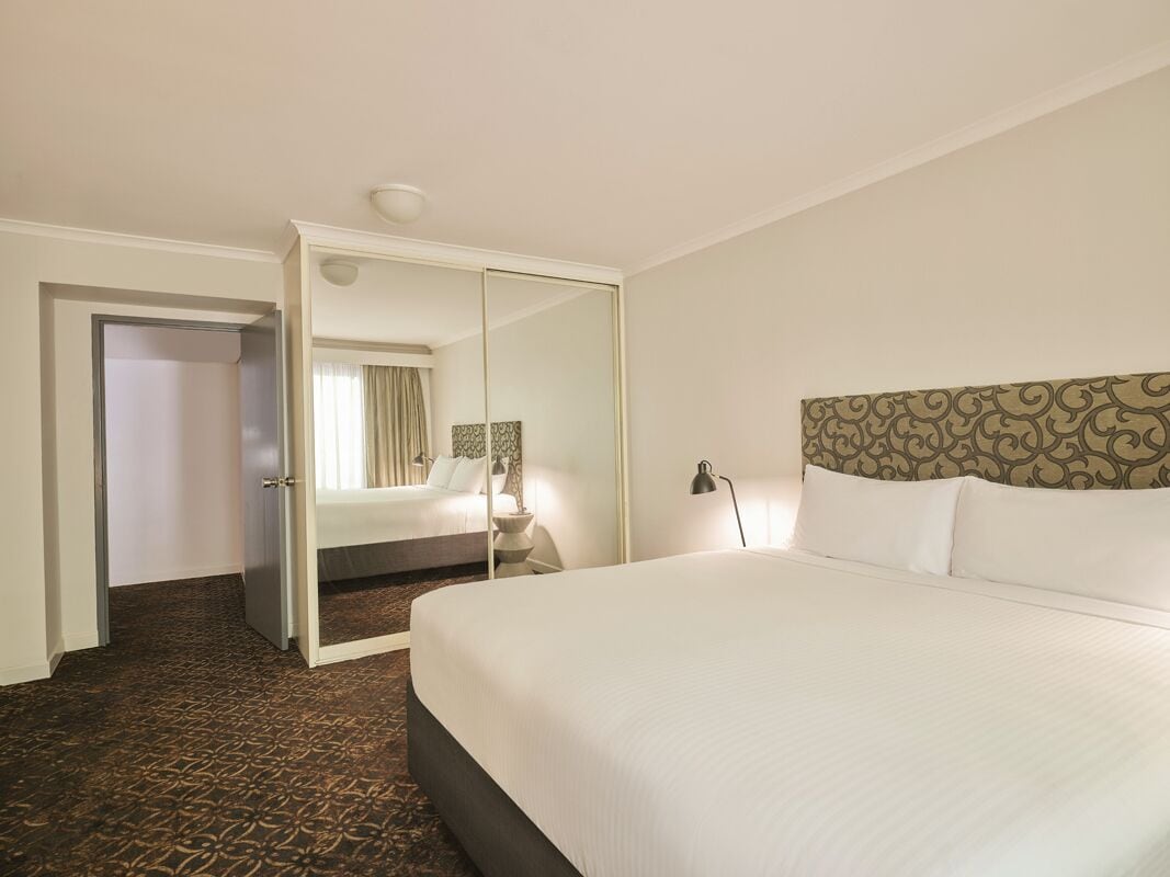 A hotel room with a large bed, a mirror, a nightstand, and a patterned carpet.