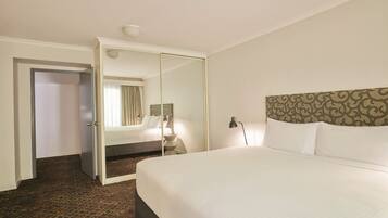 A hotel room with a large bed, a mirror, a nightstand, and a patterned carpet.