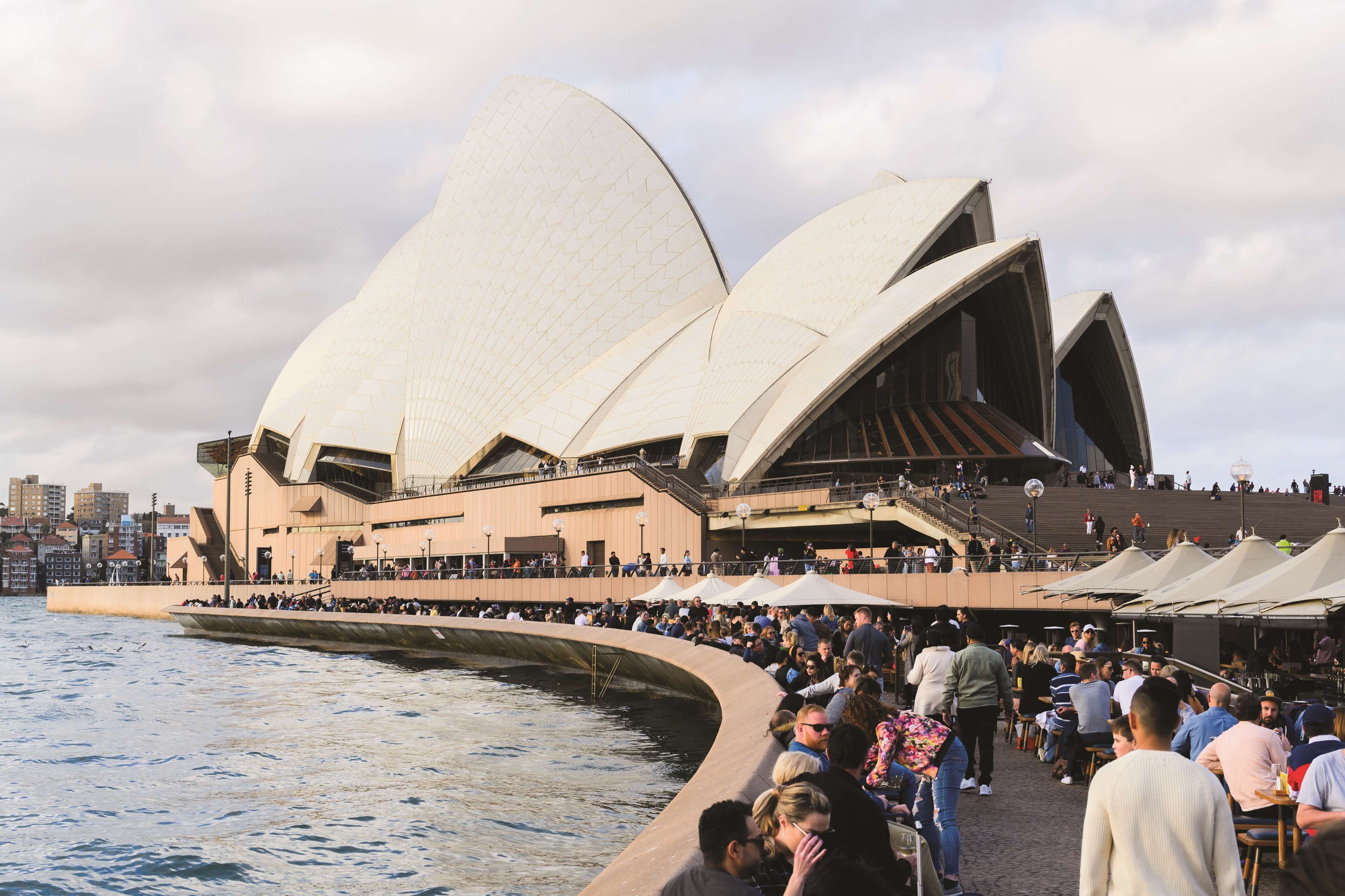 Het Sydney Opera Huis met een menigte mensen aan het water.