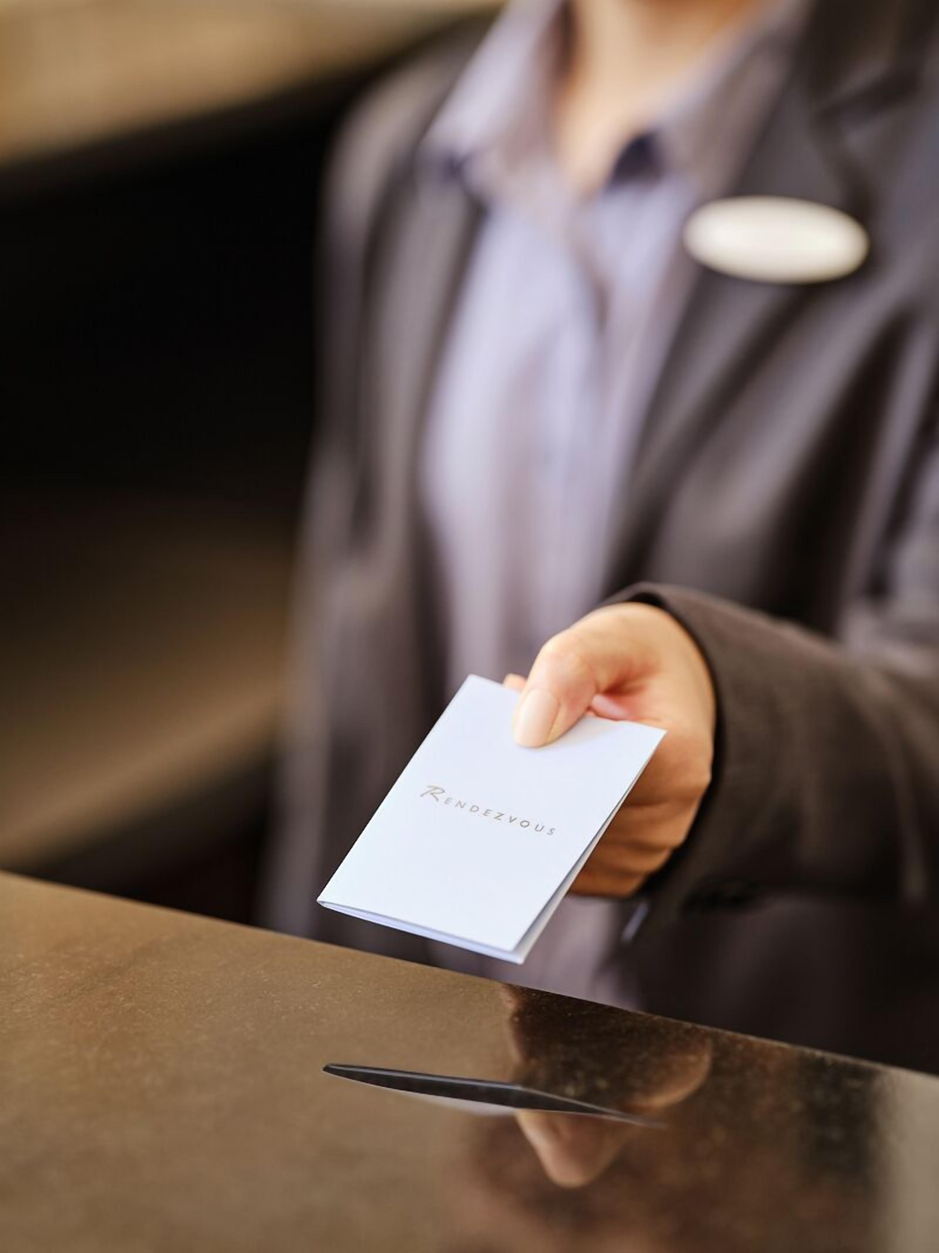 A person holding a card with "Rendezvous" written on it, standing at a reception desk.