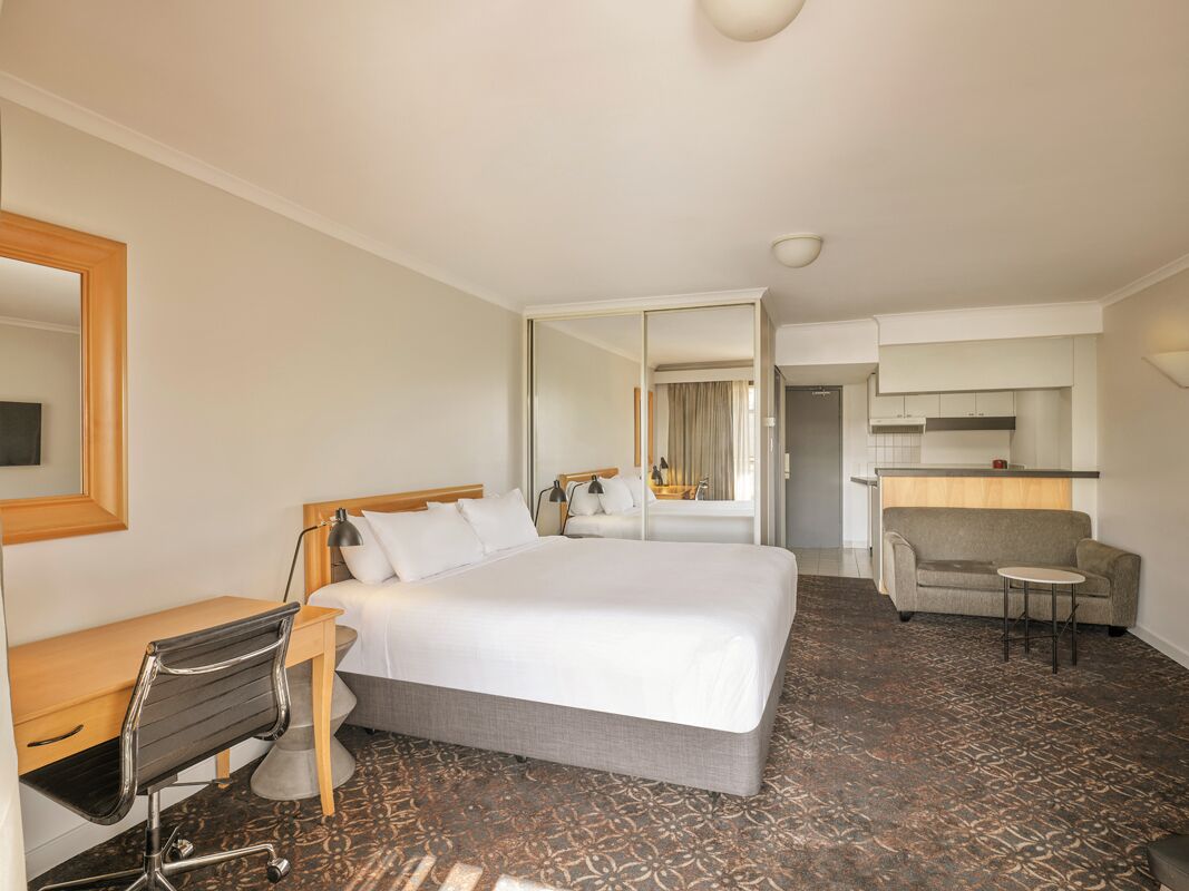 A hotel room with a large bed, a desk, a chair, a sofa, and a small table.