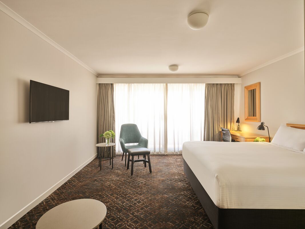 A hotel room with a bed, a desk, a chair, a television, and a window with curtains.