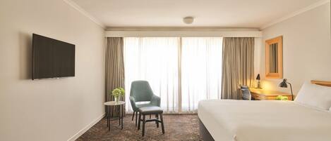 A hotel room with a bed, a desk, a chair, a television, and a window with curtains.