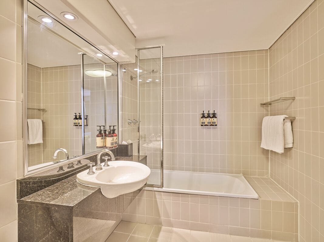 Ein modernes Badezimmer mit einer gläsernen Duschkabine, einem Waschbecken mit Marmorplatte und einer Badewanne.