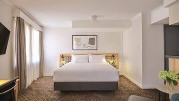 Een hotelkamer met een groot bed, een bureau, een stoel, een televisie en een kleine tafel met bloemen.