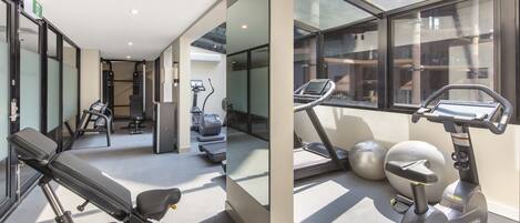A modern gym with exercise equipment, large windows, and a clean, spacious layout.